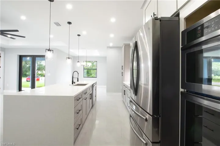Kitchen with white cabinets, hanging light fixtures, stainless steel appliances, and sink