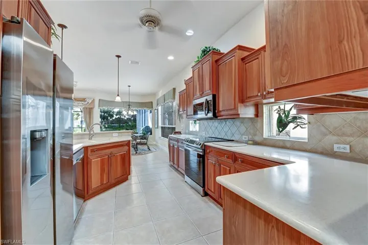 Kitchen with appliances with stainless steel finishes, tasteful backsplash, ceiling fan, light tile patterned floors, and decorative light fixtures