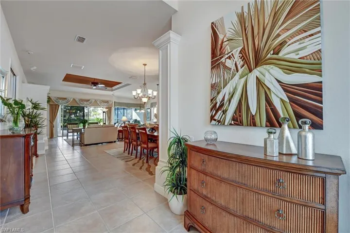 Hall with light tile patterned flooring, a tray ceiling, and an inviting chandelier