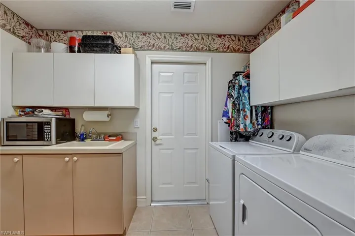 Clothes washing area featuring cabinets, light tile patterned flooring, washer and clothes dryer, and sink