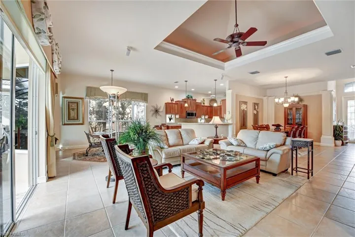 Tiled living room with a tray ceiling, crown molding, and ceiling fan with notable chandelier
