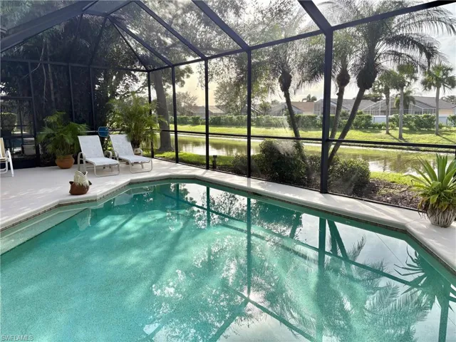 View of swimming pool with glass enclosure, a patio area, and a water view