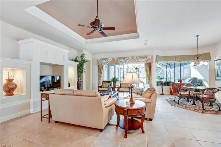 Tiled living room with a raised ceiling and ceiling fan with notable chandelier