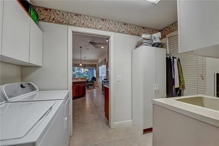 Washroom with cabinets, ceiling fan with notable chandelier, sink, independent washer and dryer, and light tile patterned flooring