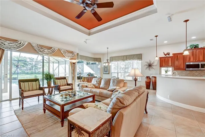Tiled living room featuring ceiling fan with notable chandelier, a raised ceiling, and ornamental molding