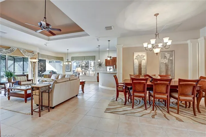 Tiled dining space with a tray ceiling, decorative columns, and ceiling fan with notable chandelier