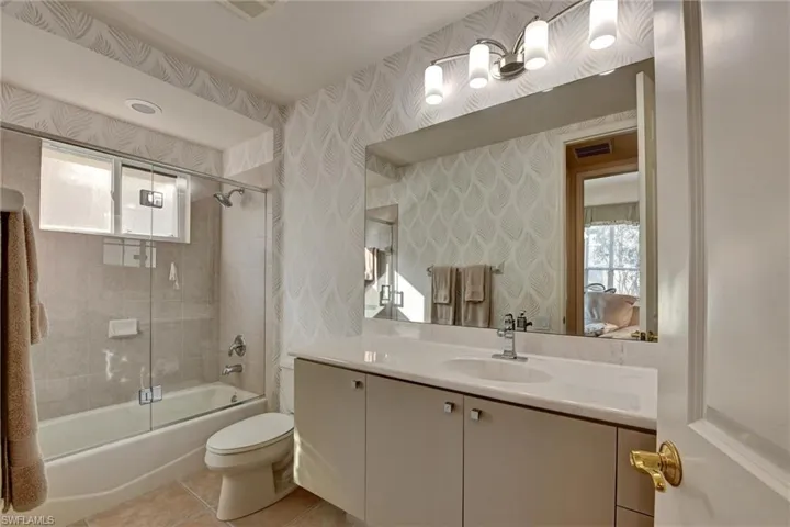 Full bathroom with toilet, vanity, tile patterned floors, and enclosed tub / shower combo