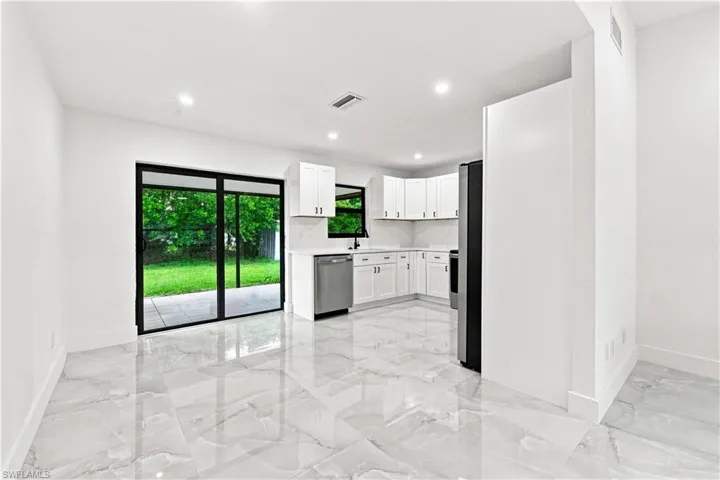 Kitchen featuring white shaker-style cabinetry, stainless steel appliances, polished stone-finish flooring, and black-framed sliding glass doors