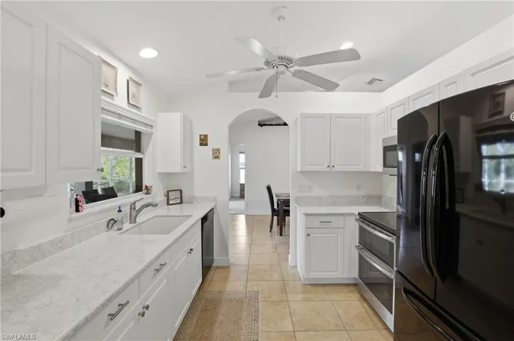 Kitchen with appliances with stainless steel finishes, arched walkways, white cabinets, recessed lighting, and light stone counters