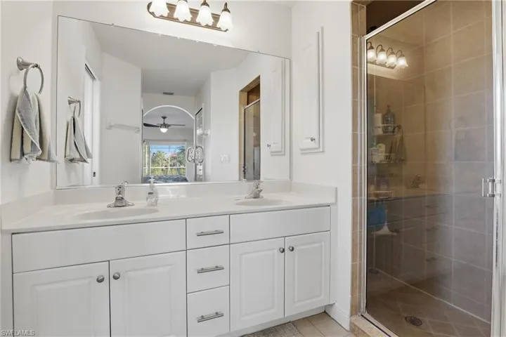Bathroom featuring double vanity, a shower stall, ceiling fan, and light tile patterned floors