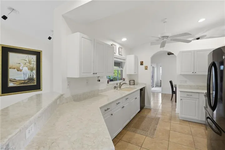 Kitchen with white cabinets, freestanding refrigerator, arched walkways, ceiling fan, and lofted ceiling