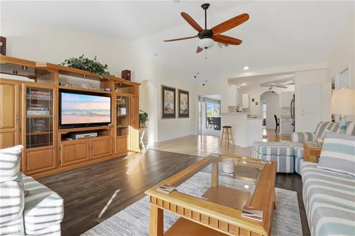 Living area with lofted ceiling, arched walkways, dark wood finished floors, and a ceiling fan
