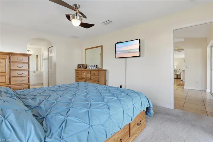 Bedroom featuring arched walkways, light colored carpet, ceiling fan, connected bathroom, and light tile patterned flooring