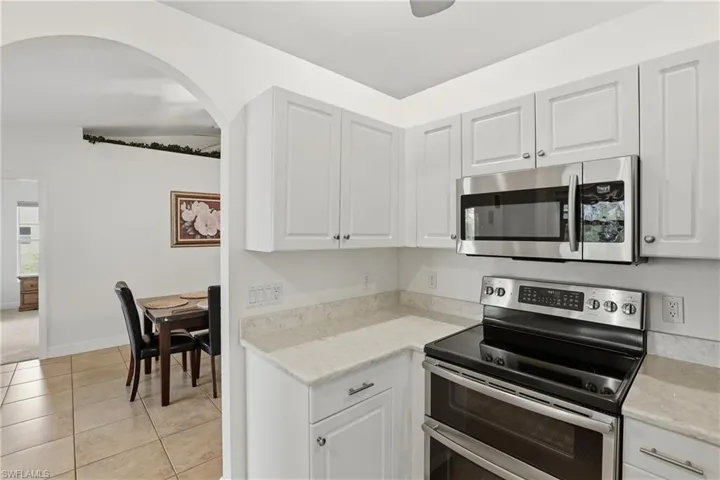 Kitchen with appliances with stainless steel finishes, light tile patterned floors, white cabinetry, and light stone counters
