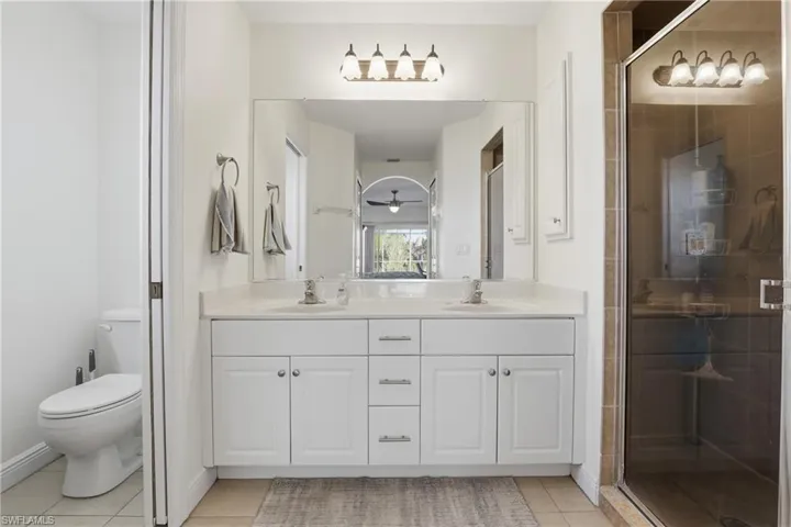 Full bath with double vanity, a shower stall, light tile patterned flooring, and ceiling fan