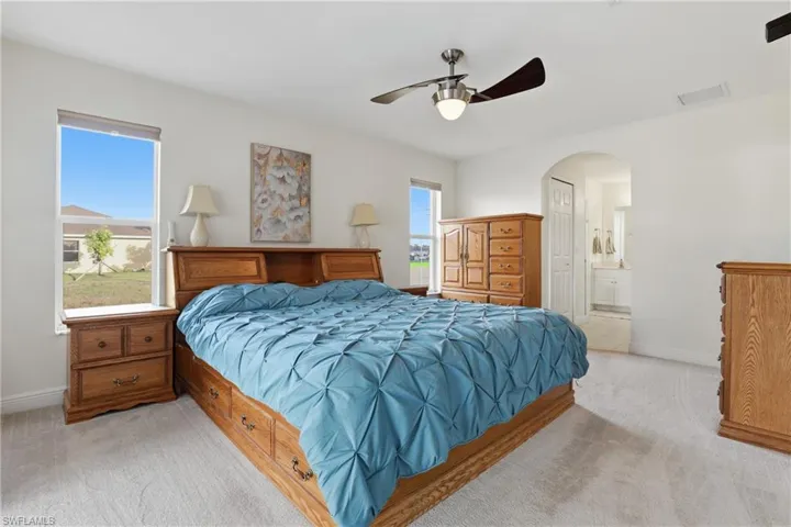 Bedroom with light carpet, ensuite bathroom, arched walkways, and a ceiling fan