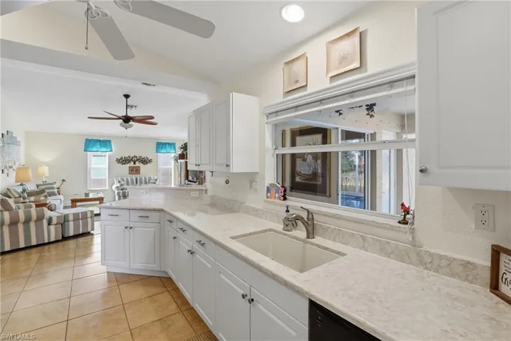 Kitchen featuring open floor plan, white cabinetry, light tile patterned floors, lofted ceiling, and light stone counters
