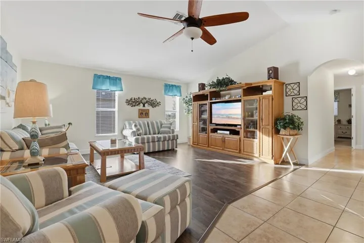 Tiled living area with a ceiling fan, lofted ceiling, and arched walkways