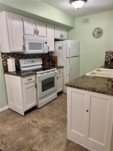Kitchen featuring white appliances, decorative backsplash, white cabinets, and a textured wall