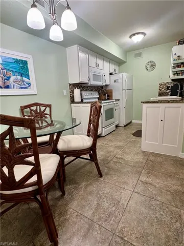Kitchen featuring white cabinetry, backsplash, white appliances, and hanging light fixtures