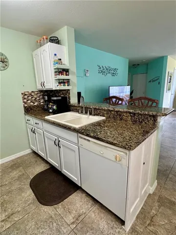 Kitchen with a breakfast bar, white cabinets, dishwasher, a peninsula, and dark stone counters
