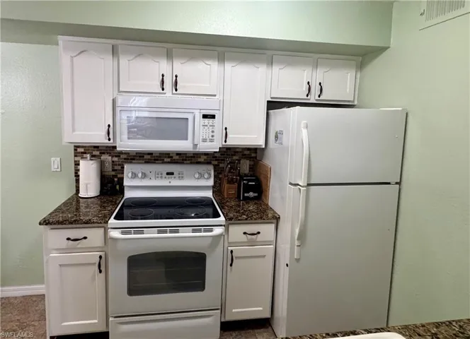 Kitchen featuring white appliances, white cabinets, a textured wall, decorative backsplash, and dark stone countertops