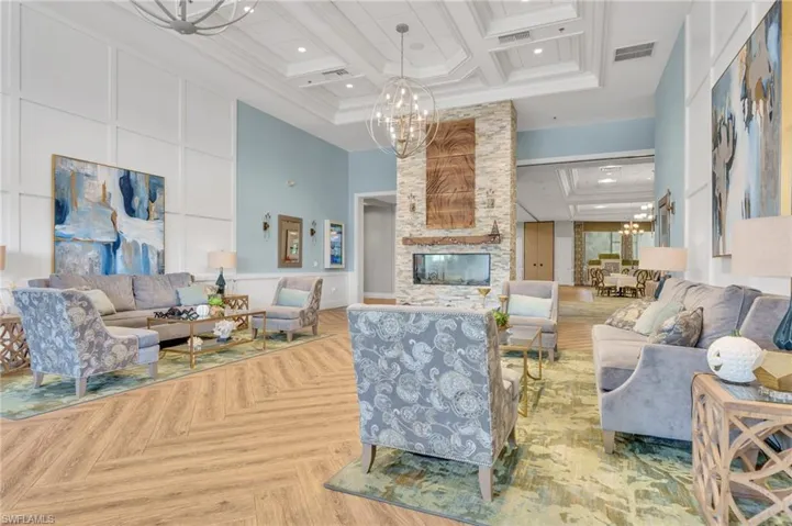 Great room featuring wood-finish flooring in a herringbone pattern, coffered ceilings with recessed lighting, stacked stone fireplace surround, and extensive wall molding