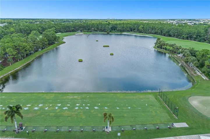 Expansive golf course landscape featuring a large lake, manicured driving range, mature palm trees, and dense perimeter foliage