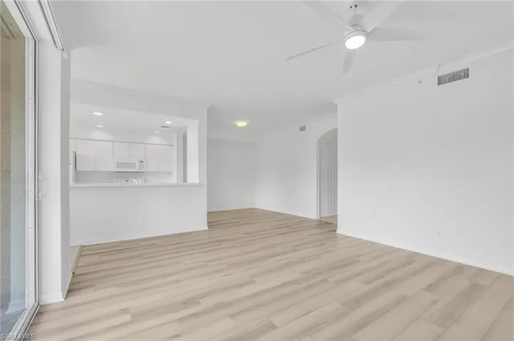 Open-concept interior featuring vinyl flooring, a ceiling fan with integrated lighting, recessed lighting, and white cabinetry in the kitchen area