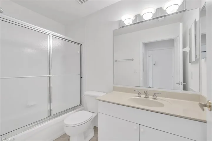 Guest Bathroom featuring a vanity with a solid-surface countertop, an integrated oval sink, a large wall-mounted mirror, a three-light fixture, and a bathtub with a sliding glass door enclosure