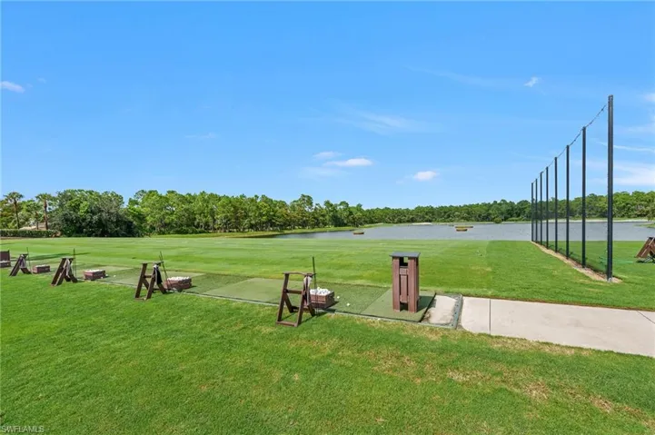 Driving range featuring synthetic turf hitting stations, protective perimeter netting, and a pond backdrop