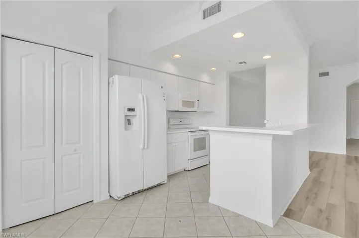 Kitchen featuring a breakfast bar, white cabinetry, integrated appliances, tile flooring, and wood-finish flooring