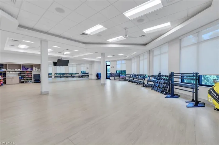 Fitness studio featuring wood-finish flooring, recessed lighting, drop ceiling, expansive wall-to-wall mirrors, and large windows with integrated roller shades