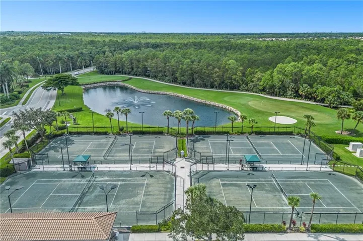 Recreational area featuring four fenced tennis courts, a decorative water feature with a fountain, and manicured landscaping