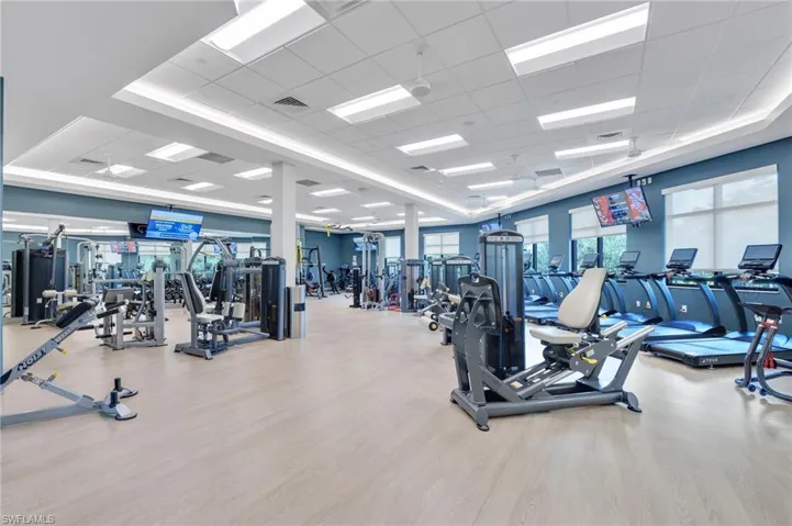 Expansive fitness center featuring recessed perimeter cove lighting, wood-finish flooring, a coffered drop ceiling, and large windows with integrated roller shades