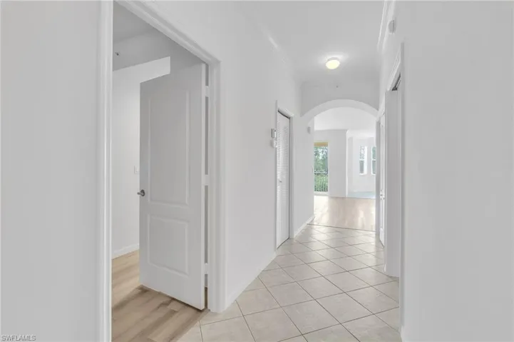 Hallway featuring neutral-toned tile flooring, recessed crown molding, arched architectural detail, and wood-finish flooring in adjoining spaces