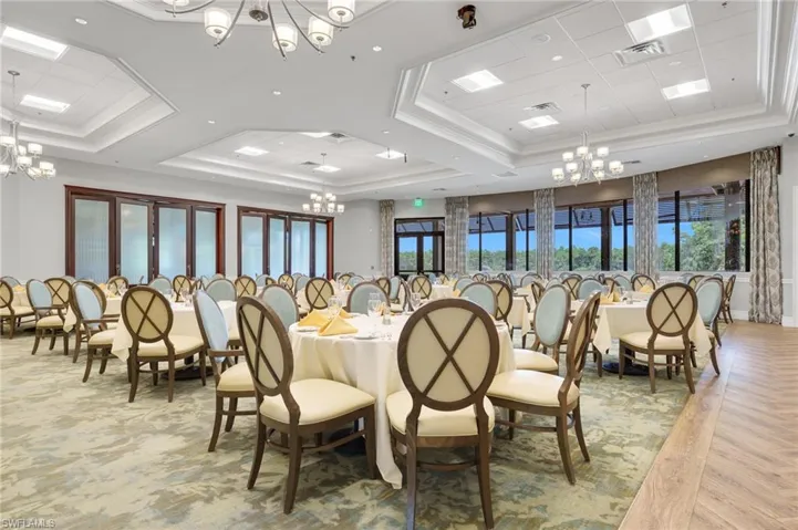 Expansive room featuring coffered tray ceilings, multiple tiered chandeliers, floor-to-ceiling windows, and wood-finish perimeter flooring