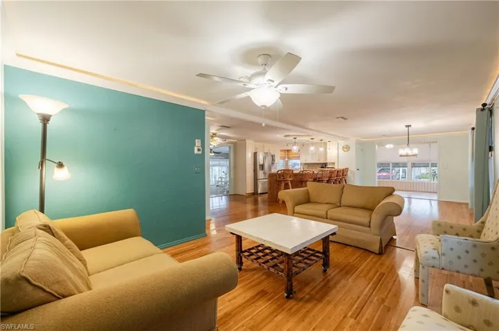 Living room with crown molding, ceiling fan with notable chandelier, and light hardwood / wood-style floors