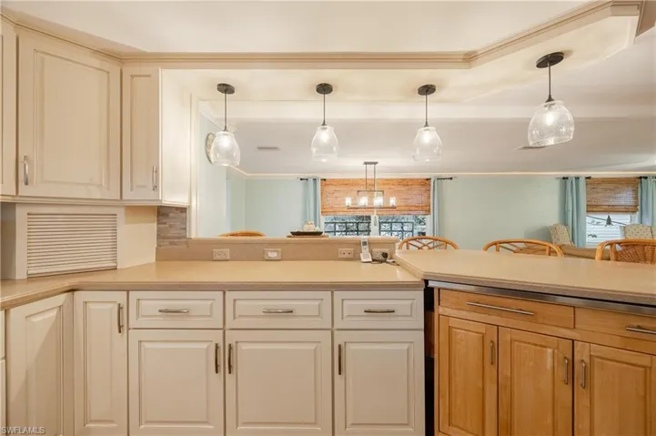 Kitchen featuring a notable chandelier, kitchen peninsula, pendant lighting, decorative backsplash, and ornamental molding