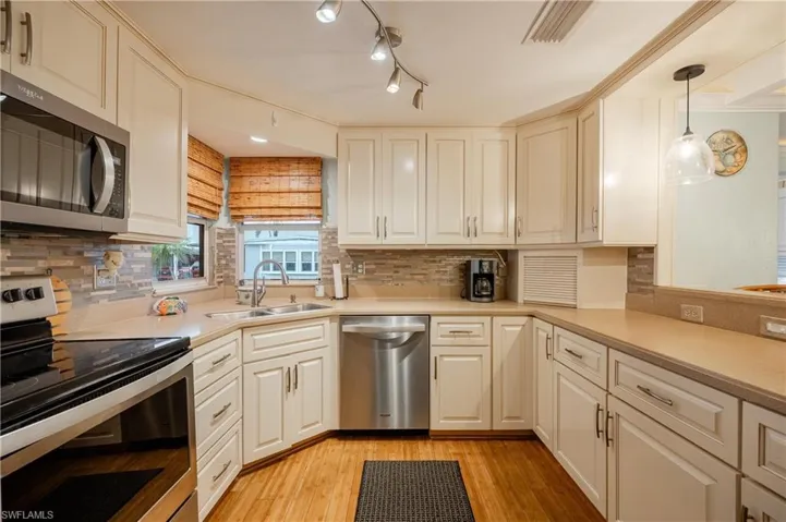 Kitchen featuring pendant lighting, light hardwood / wood-style floors, stainless steel appliances, ornamental molding, and sink