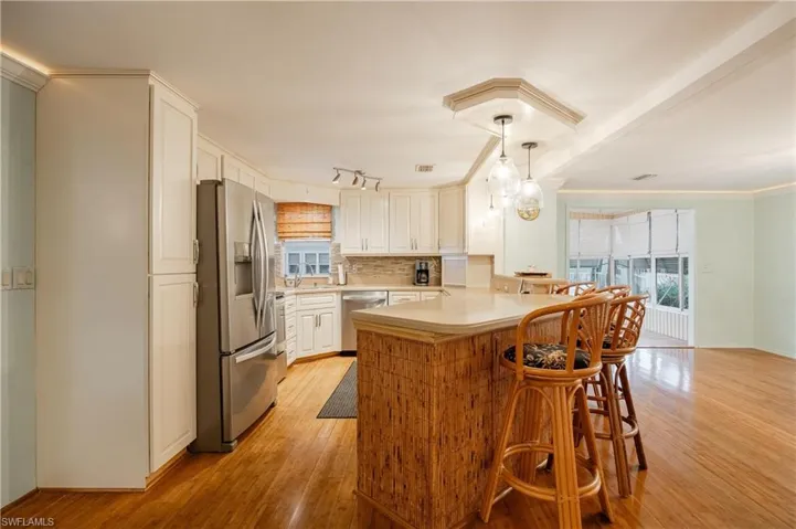 Kitchen with appliances with stainless steel finishes, tasteful backsplash, a breakfast bar, kitchen peninsula, and light wood-type flooring