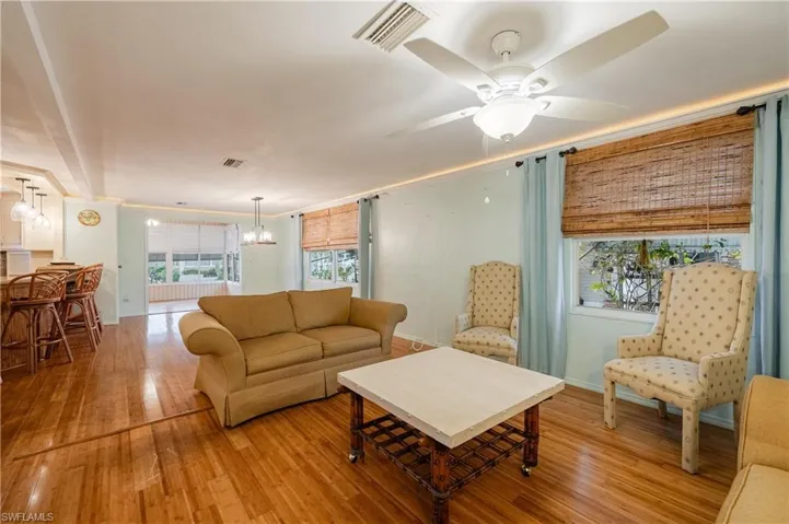 Living room with ceiling fan with notable chandelier and light wood-type flooring