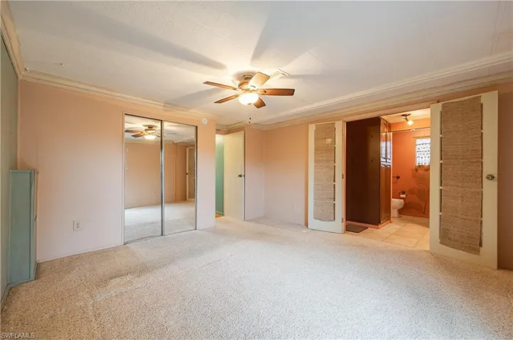 Unfurnished bedroom featuring a textured ceiling, ensuite bathroom, ornamental molding, light colored carpet, and ceiling fan