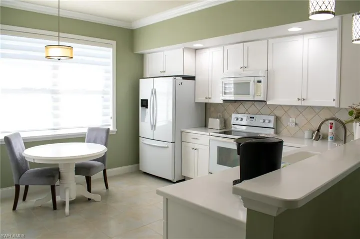 Kitchen featuring kitchen peninsula, white cabinetry, hanging light fixtures, and white appliances