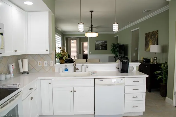 Kitchen featuring white appliances, sink, light tile patterned floors, decorative light fixtures, and white cabinets