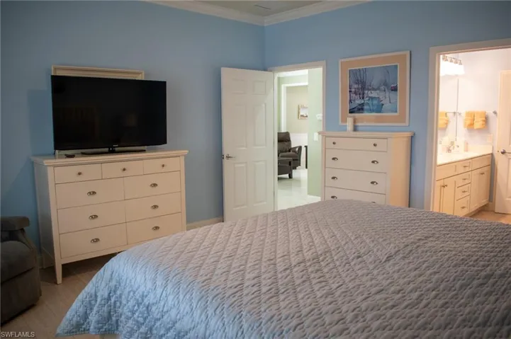Bedroom with light wood-type flooring, ensuite bath, and ornamental molding