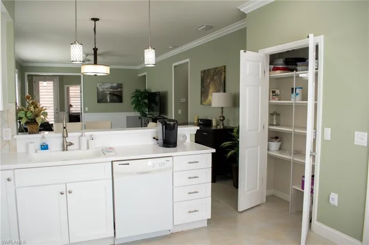 Kitchen with white cabinetry, sink, white dishwasher, decorative light fixtures, and ornamental molding