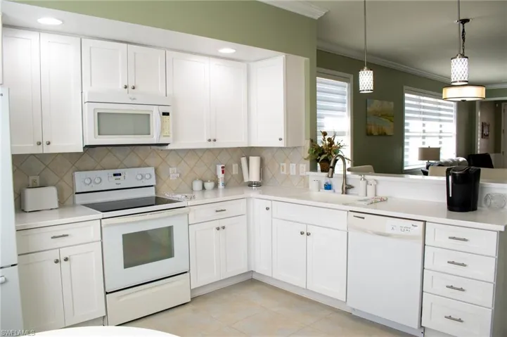 Kitchen featuring white cabinetry, sink, pendant lighting, white appliances, and light tile patterned floors