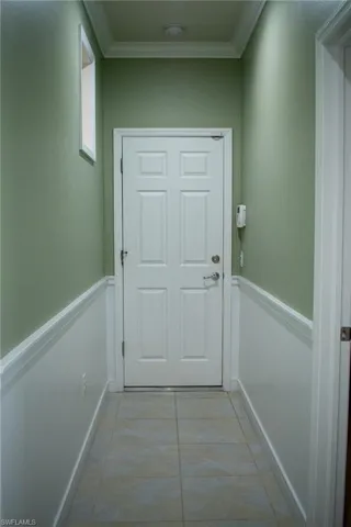 Doorway with light tile patterned flooring and crown molding
