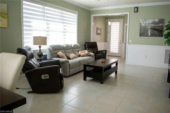 Living room featuring light tile patterned floors, ceiling fan, and crown molding